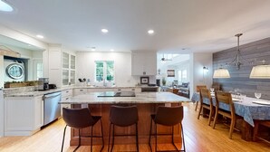 Een moderne keuken met een groot eiland, barkrukken en een eethoek met een tafel en stoelen.