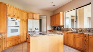 A kitchen with wooden cabinets, a granite countertop, and stainless steel appliances. - Firefly by AvantStay | Spacious Backyard w/ Pool& Hot Tub! (La Quinta)