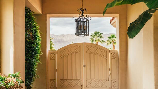 A gated entrance with a view of mountains and palm trees. - Firefly by AvantStay | Spacious Backyard w/ Pool& Hot Tub! (La Quinta)