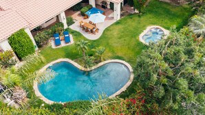 A pool with a heart-shaped design, a patio area with a table and chairs, and a covered seating area. - Firefly by AvantStay | Spacious Backyard w/ Pool& Hot Tub! (La Quinta)