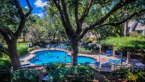 Una piscina circondata da alberi e poltroncine da relax blu.