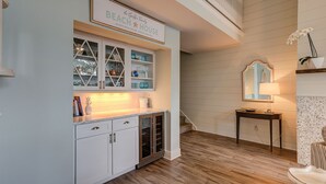 Una cucina con mobili bianchi, pavimento in legno e un cartello sopra il bancone con la scritta 'BEACH HOUSE'.