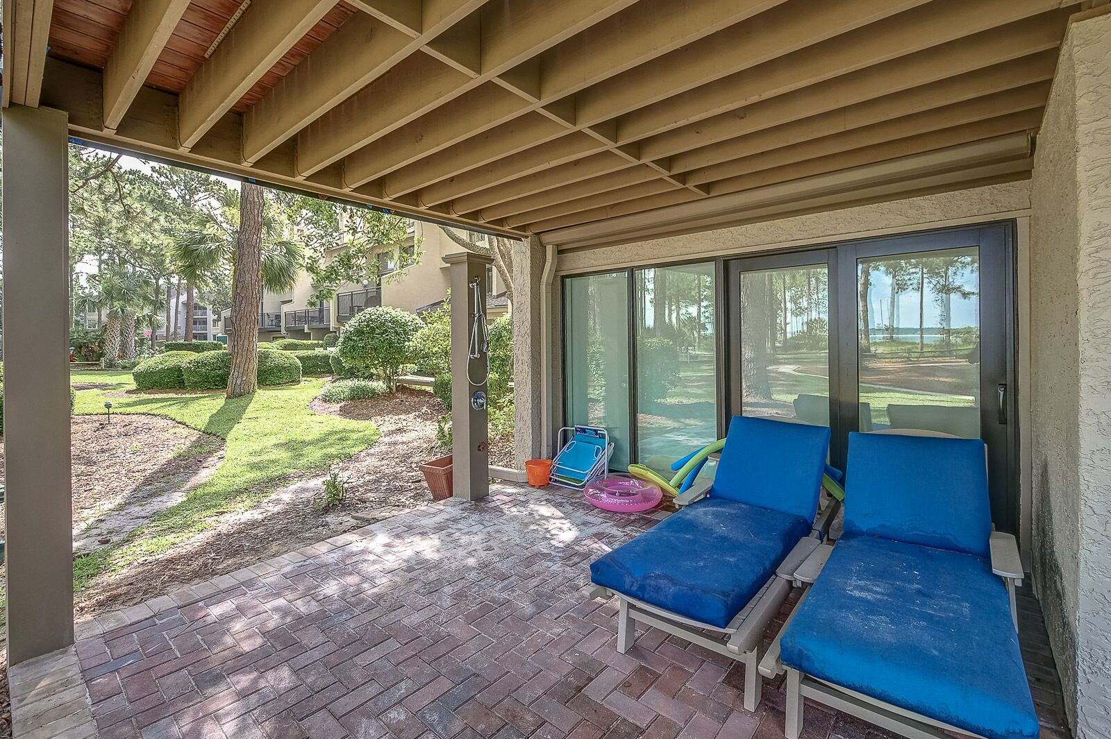 Un patio couvert avec deux fauteuils de jardin bleus, une petite table de billard et une vue sur le jardin.