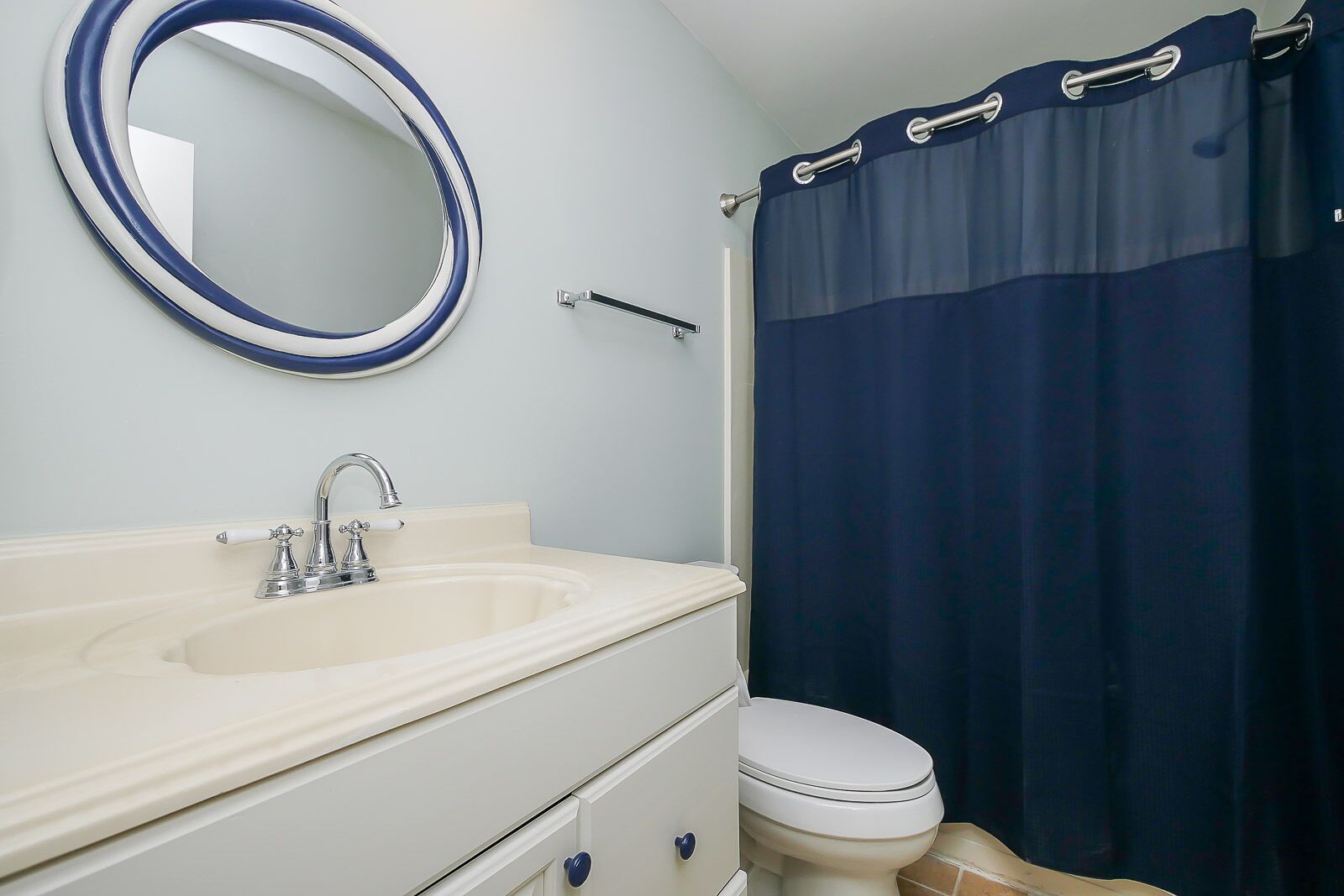 Baño con lavamanos, espejo, inodoro y cortina de ducha azul.