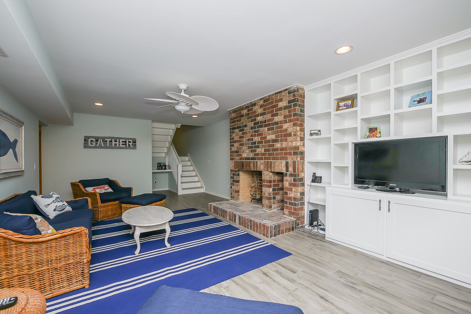 A living room with a fireplace, wicker furniture, a TV, and a staircase.