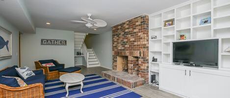A living room with a fireplace, wicker furniture, a TV, and a staircase.