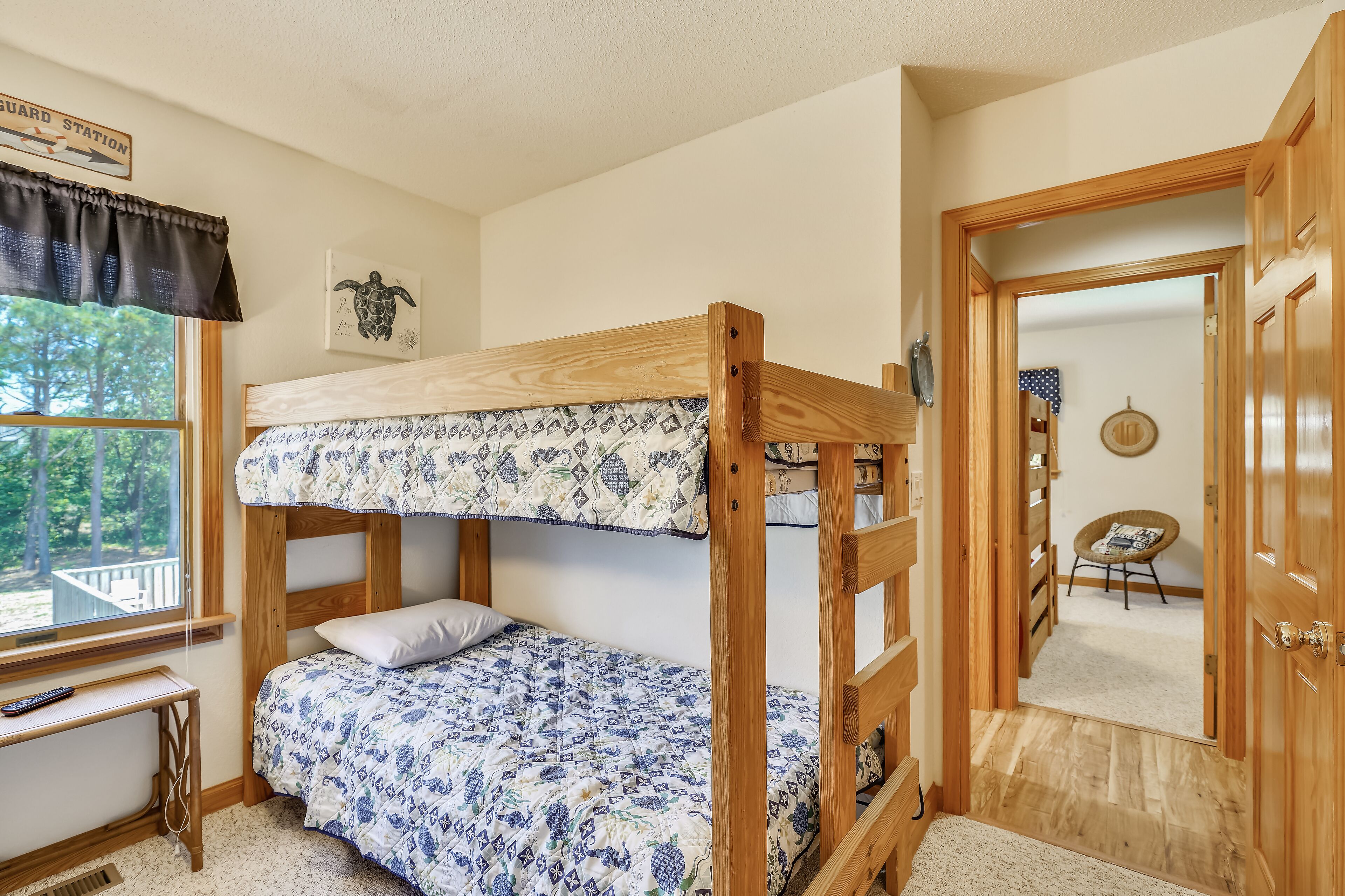 A bunk bed room with a window, a desk, and a door leading to another room.