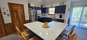 Uma cozinha com bancada de mármore, cadeiras de madeira, geladeira de aço inoxidável e armários azul escuro.