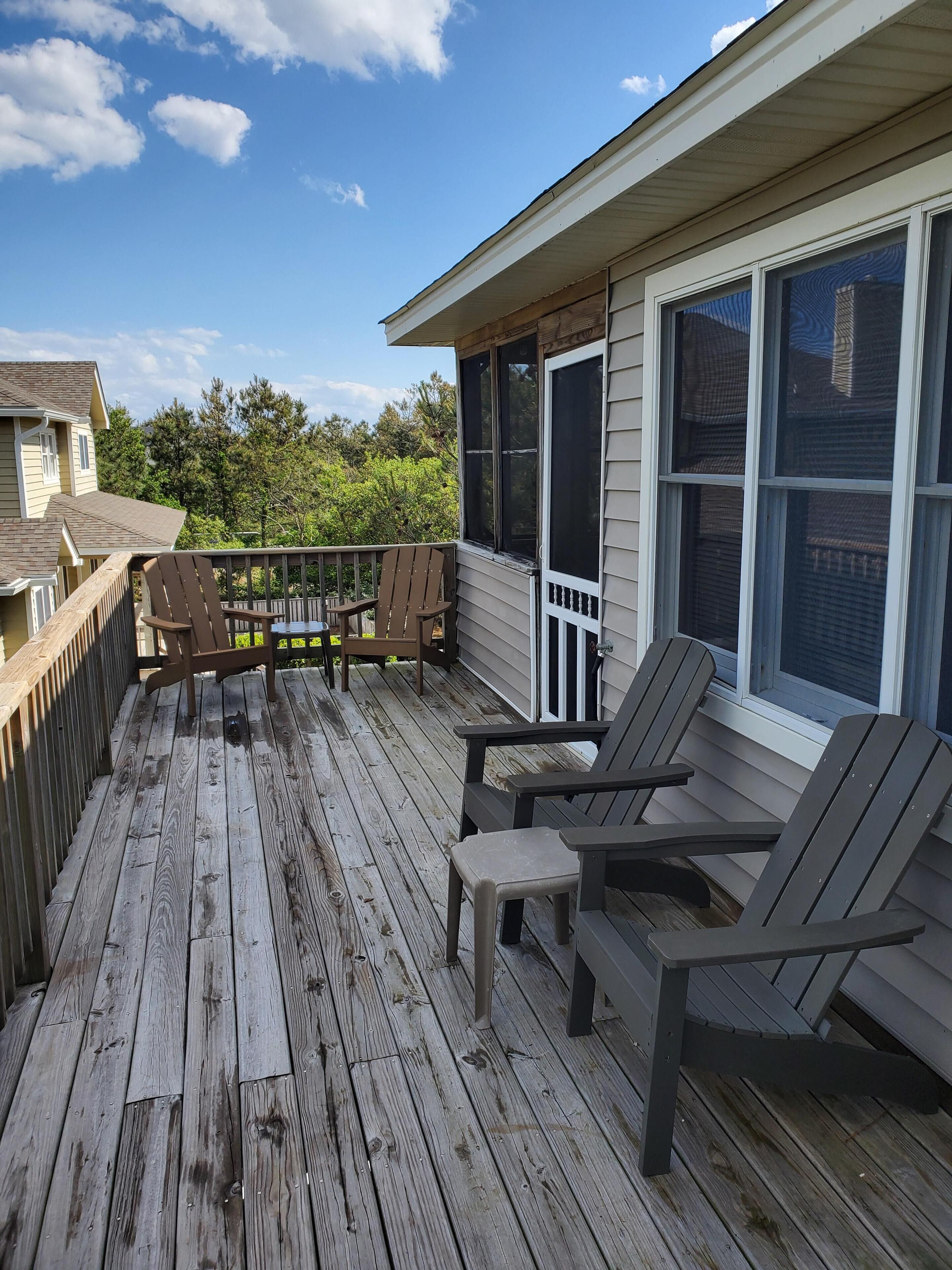 A wooden deck with two Adirondack chairs and a small table, overlooking a residential area with trees and houses.