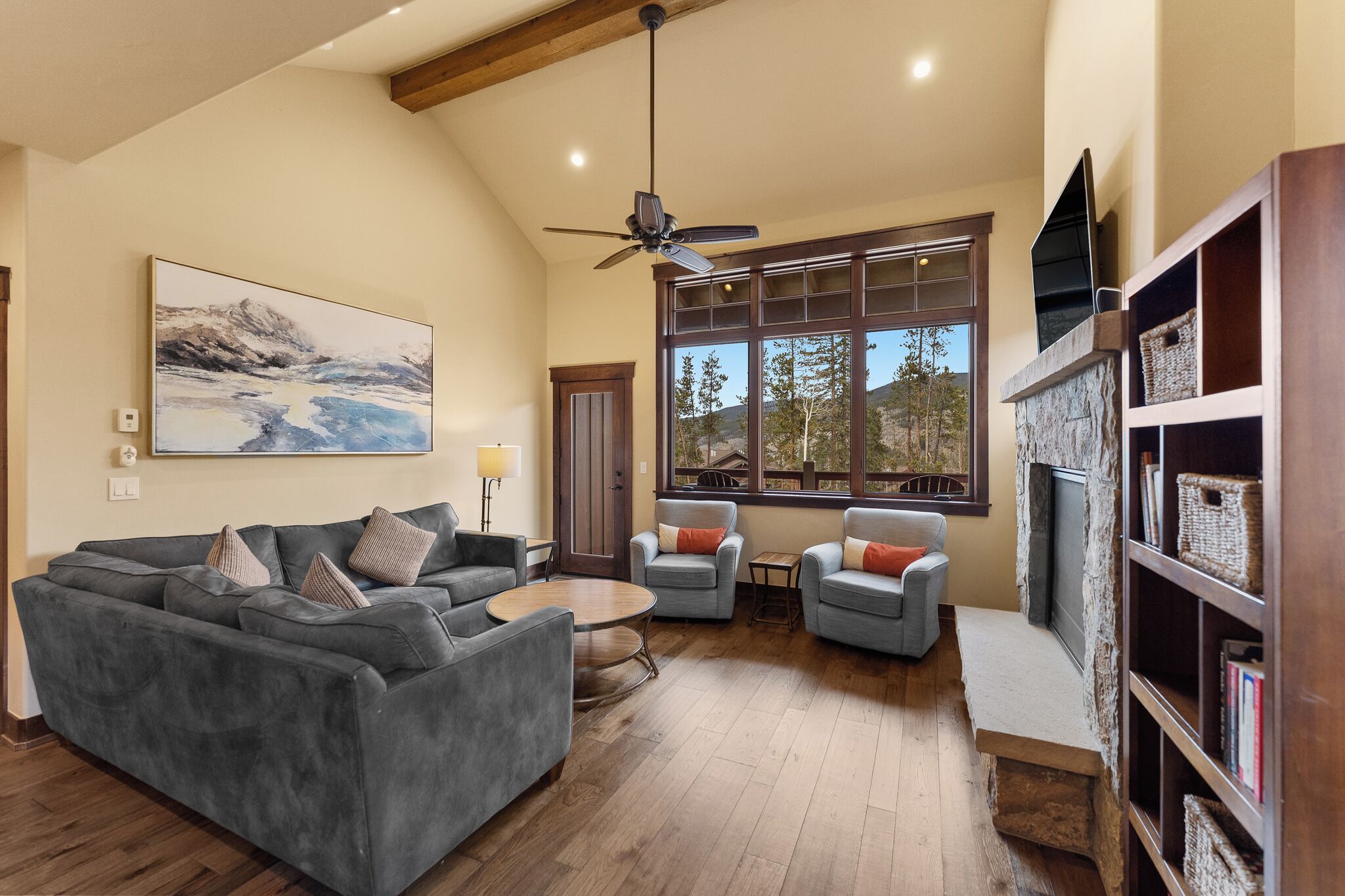 A spacious living room with a gray sectional sofa, two armchairs, a small round table, and a fireplace.