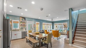 A spacious kitchen with a dining area, a staircase, and a living room with a sofa and chairs. - Pura Vida Cottage! Community Pool, Downtown PA! (Port Aransas)