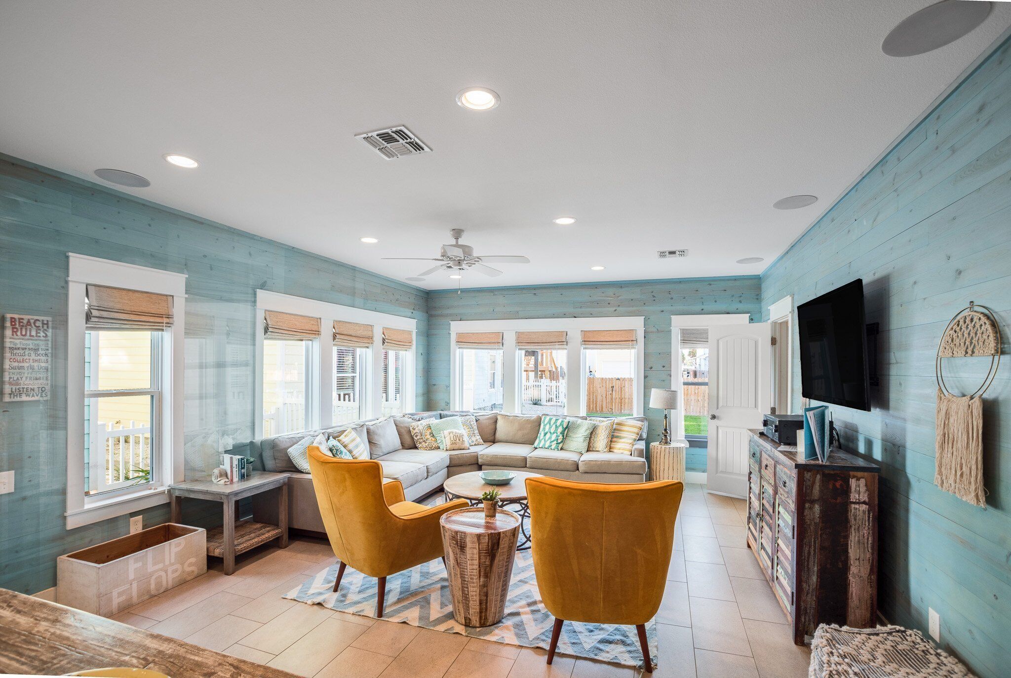 A spacious living room with a large sectional sofa, two yellow armchairs, a coffee table, and a television on a wooden cabinet.