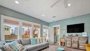 A spacious living room with a grey sectional sofa, a wooden coffee table, and a television mounted on the wall. - Pura Vida Cottage! Community Pool, Downtown PA! (Port Aransas)
