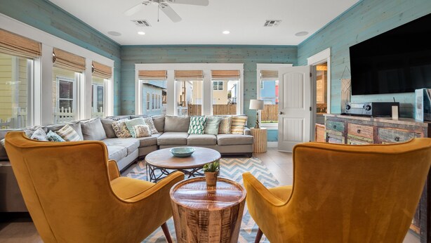 A living room with a sofa, yellow chairs, a coffee table, and a television. - Pura Vida Cottage! Community Pool, Downtown PA! (Port Aransas)