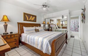 A bedroom with a wooden bed, bedside lamps, a ceiling fan, and a large mirror.