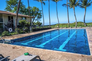 A swimming pool with clear blue water, surrounded by palm trees and a building with a balcony.