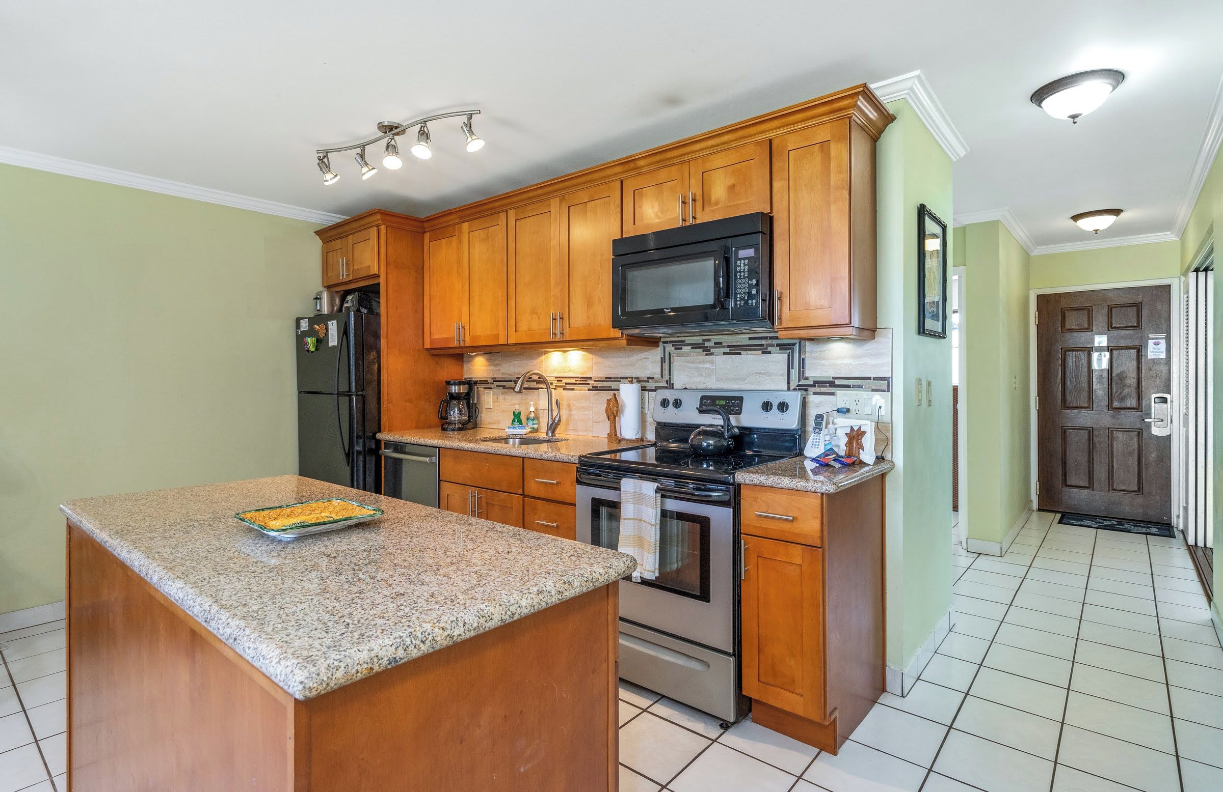 A kitchen with wooden cabinets, a granite countertop, a stainless steel refrigerator, a microwave, a stove, and a sink.