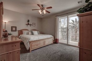 A bedroom with a bed, a ceiling fan, a window with a view, and a wooden dresser.