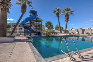 A swimming pool with a water slide and palm trees.