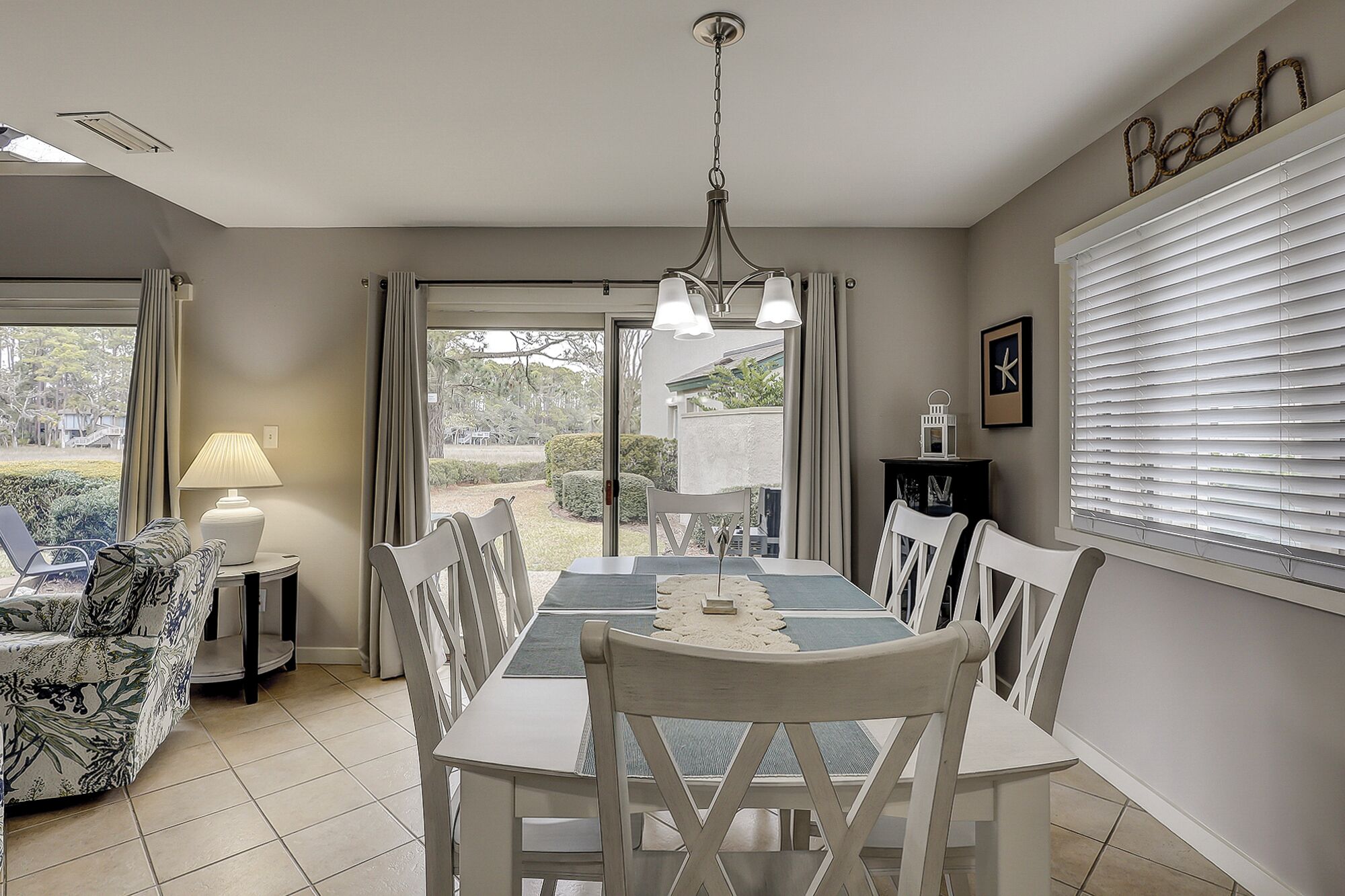 Un coin repas comprenant une table et des chaises, une lampe, et une vue sur l’extérieur par une porte vitrée.