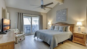 Een slaapkamer met een bed, een bureau, een stoel, een plafondventilator, een televisie en een raam met gordijnen.