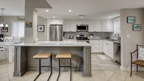 Een moderne keuken met witte kasten, roestvrijstalen apparatuur en een centraal kookeiland met krukken.