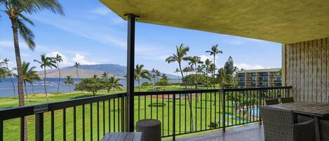 Un balcon avec vue sur une piscine, des palmiers et des montagnes.