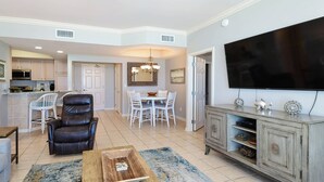 A living room with a leather chair, a coffee table, a TV, and a dining area with a table and chairs. - Comfortable Beachfront Condo w/ Easy Beach Access in Central Destin! 🏖☀🌴 (Destin)