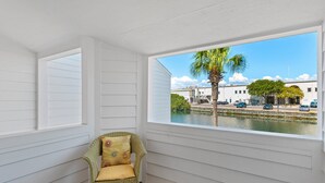 A room with a view of a body of water, a chair, and a window with white shutters. - 🏖️Shoreline TH 4-3 | Steps to Beach+Seasonal Chairs (Destin)