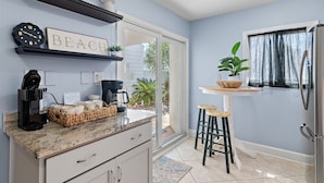 A kitchen with a granite countertop, a coffee maker, a basket of bread, and a sign that reads "BEACH HAPPY." - 🏖️Shoreline TH 4-3 | Steps to Beach+Seasonal Chairs (Destin)