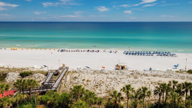 A beach with a wooden boardwalk, beach umbrellas, and a lifeguard tower. - 1BR w/ Beach Views! Spacious Balcony, Tropical Pool, Tiki Bar, Hot Tub, Tram. (Miramar Beach)