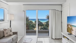 A room with a balcony, a sofa, a coffee table, and a TV. - 1BR w/ Beach Views! Spacious Balcony, Tropical Pool, Tiki Bar, Hot Tub, Tram. (Miramar Beach)