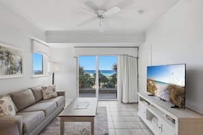 Una sala de estar moderna con un sofá, una mesa de centro, un televisor y un balcón con vista a la playa.