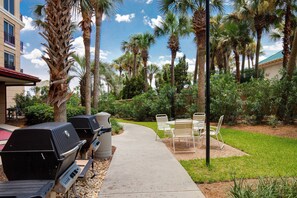 A patio with outdoor grills, chairs, and a pathway. - 1BR w/ Beach Views! Spacious Balcony, Tropical Pool, Tiki Bar, Hot Tub, Tram. (Miramar Beach)