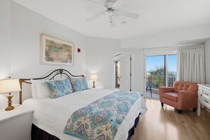 A bedroom with a bed, a chair, a ceiling fan, a door leading to a balcony, and a painting on the wall. - 1BR w/ Beach Views! Spacious Balcony, Tropical Pool, Tiki Bar, Hot Tub, Tram. (Miramar Beach)