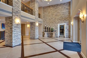 Enter a spacious lobby with a high ceiling and modern design, featuring a geometric tile floor and stone pillars.