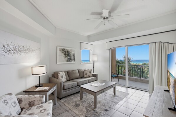 A modern living room with a sofa, coffee table, and a TV on a balcony overlooking the ocean. - 1BR w/ Beach Views! Spacious Balcony, Tropical Pool, Tiki Bar, Hot Tub, Tram. (Miramar Beach)