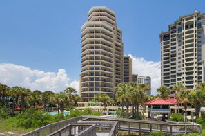 A high-rise hotel with multiple balconies, a pool area, and surrounding greenery. - 1BR w/ Beach Views! Spacious Balcony, Tropical Pool, Tiki Bar, Hot Tub, Tram. (Miramar Beach)