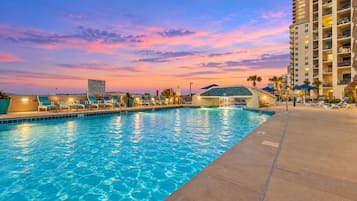 A swimming pool with lounge chairs and a hotel building in the background.
