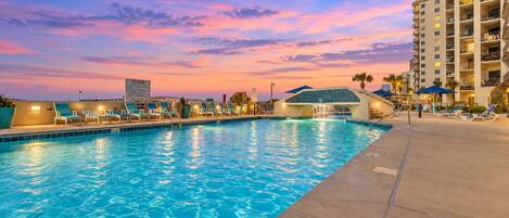 A swimming pool with lounge chairs and a hotel building in the background.