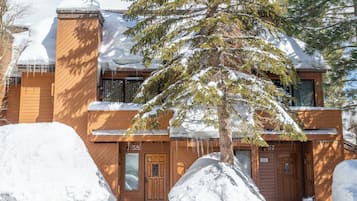 A wooden cabin with a snow-covered roof and a large tree in front.
