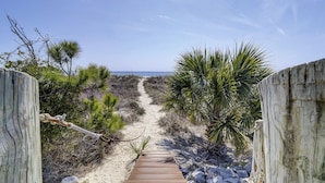 A wooden boardwalk leading to a beach, surrounded by sand dunes and sparse vegetation.