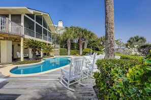 A poolside area with a wooden deck, lounge chairs, and a building with a balcony. - 13 Dune Lane - Oceanfront, Large Screened Porch and Private Pool (Hilton Head Island)