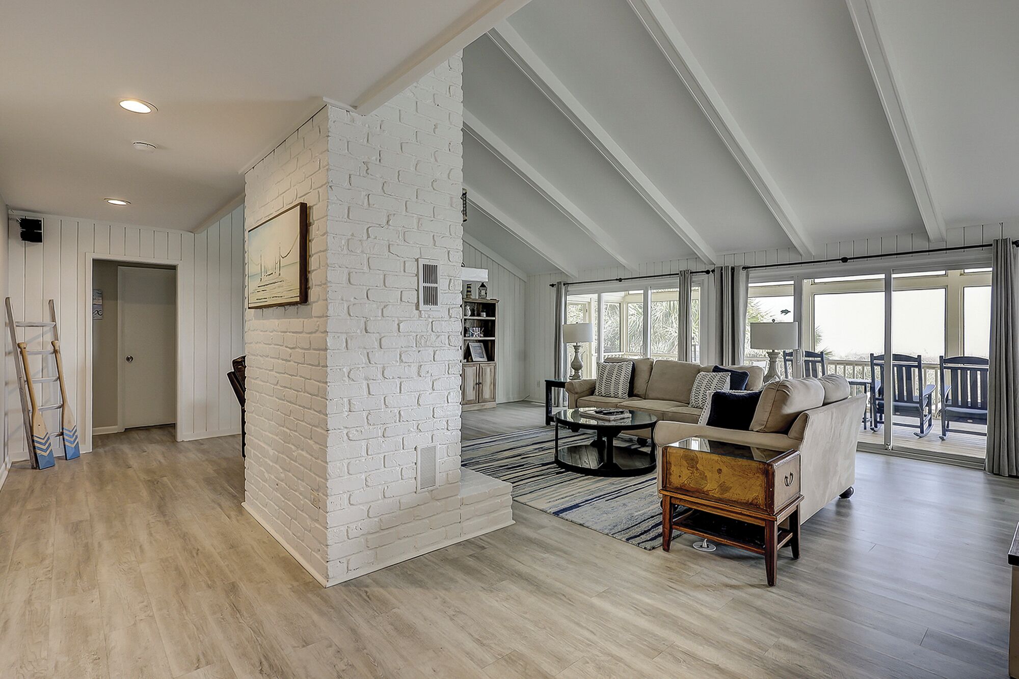A spacious living area with a white brick accent wall, a sofa set, a coffee table, and a view to a balcony.