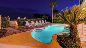 A swimming pool with lounge chairs and palm trees at night.