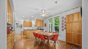 Une cuisine spacieuse avec des meubles de rangement en bois, une table à manger avec des chaises rouges et un ventilateur de plafond.