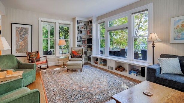 Een ruime woonkamer met een groot raam, een inbouwboekenplank, een groene fauteuil, een kamerkleed met een patroon en een houten salontafel.