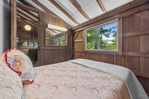 A bedroom with a large bed, wooden walls, a skylight, and a view of greenery outside.