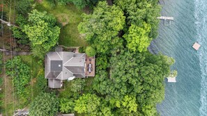 A house with a sloped roof, surrounded by dense green trees, near a body of water with docks.