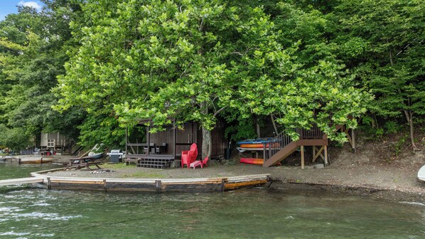 A lakeside cabin with a dock, outdoor seating, and a boat storage area.
